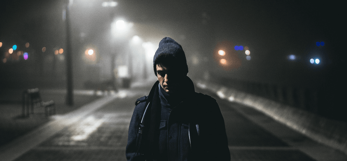 Image of a man wearing jacket and beanie walking alone on a dark night under the light posts.